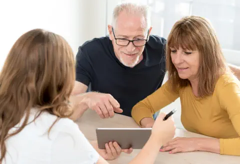 A middle aged couple is being shown information on a tablet by a staff member